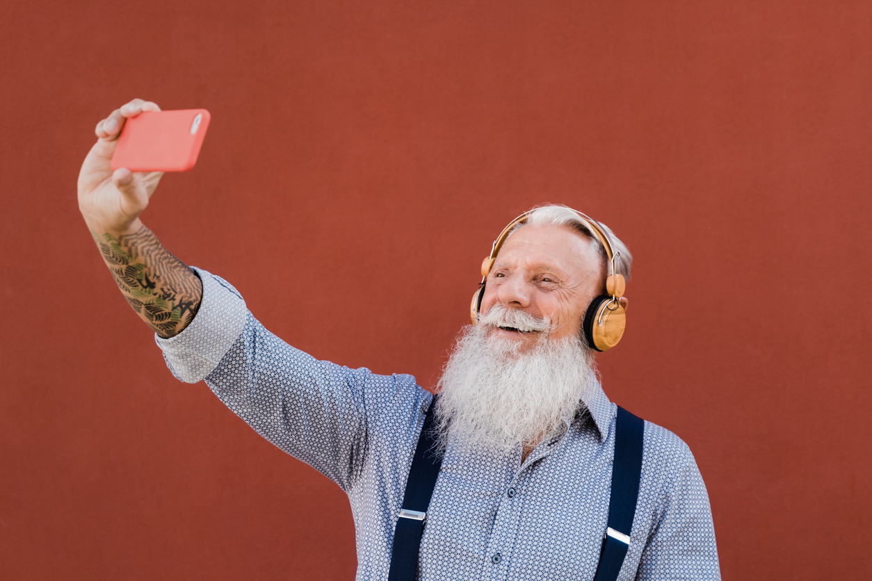 Happy senior hipster man listening music on smartphone app outdoors in the city - Tech and joyful elderly lifestyle concept - Focus on face